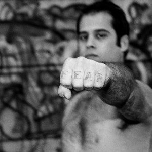 A man holding his fist towards the camera with the word 'fear' tattooed on his fingers